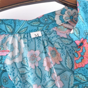Close-up of floral print dress V-neckline with size M label on blue bohemian fabric