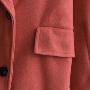 Close-up detail of warm pink wool coat showing stitching, black button, and flap pocket