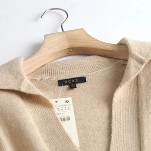 Detailed view of beige V-neck knit polo neck and branded label with size tags