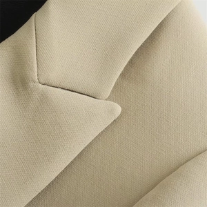 Macro detail of the beige blazer's notched lapel showing textured fabric and neat stitching