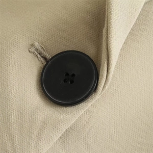 Close-up of a black four-hole button on solid beige long-sleeve oversized blazer for women