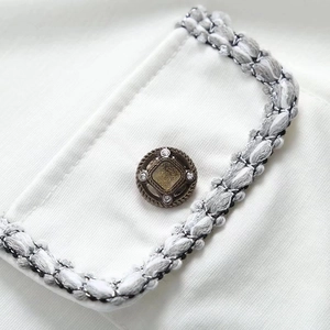 Detail of white tweed-style short sleeve shirt showing metallic button and woven trim