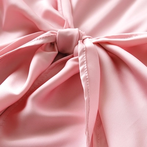 Close-up of pink satin long sleeve dress showing pleated waist and lace-up bow detail