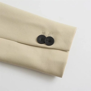 Close-up of beige twill blazer sleeve with dual black decorative buttons and fine stitching