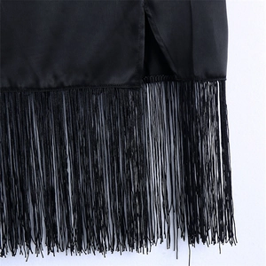 Détail de l'ourlet de la jupe en satin noir avec de longues franges et une fente latérale