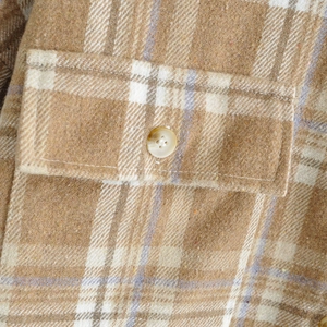 Detalle de una camisa de franela a cuadros caqui con bolsillo y cierre de botón