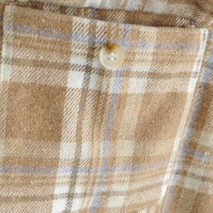 Detalle de camisa de cuadros caqui con textura de lana y botón de resina decorativo