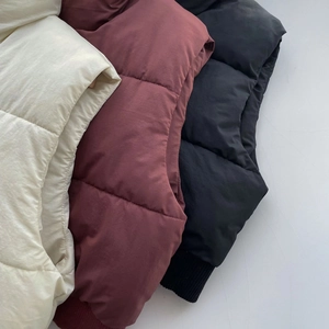 Détail de gilets matelassés en beige, bordeaux et noir avec finitions à ourlet côtelé