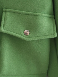Macro detail of green wool coat showing flap pocket with silver metal button and texture