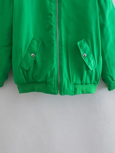 Detailed shot of green bomber jacket featuring metal zipper and flap pockets with buttons