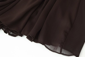 Detailed macro view of sheer pleated fabric and fine hem stitching on dark brown skirt