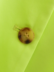 Macro detail of amber button and fine woven fabric on lime green casual blazer