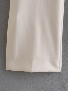 Close-up of beige high-waist trousers showing the fine woven texture and hem detail