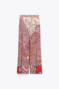Détail d'un pantalon taille haute à motif paisley coloré et bordures rouges au bas des jambes