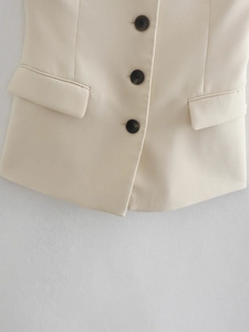 Beige sleeveless vest top with three dark buttons and flap pockets detail view