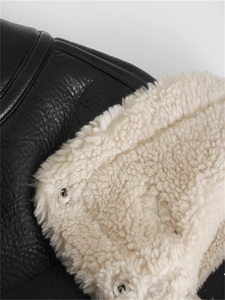 Detail of black faux leather texture and white faux shearling lining with silver metal snap