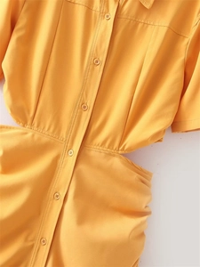 Detailed view of the bright yellow waist cutout and pleated fabric on the dress
