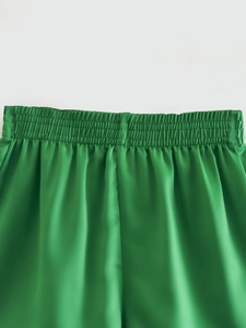 Detail of green satin high-waisted shorts featuring a wide elastic shirred waistband