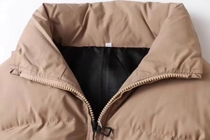 Close-up of stand-up collar with smooth zipper and black lining on khaki puffer jacket