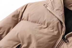 Detail of khaki puffer jacket showing stand-up collar and black metal zipper closure