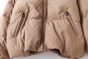 Detail of khaki puffer jacket showing metal zipper and matching zippered pockets