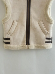 Detail of faux shearling vest featuring brown leather trim and metal side buckles