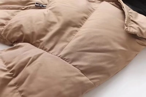 Detailed close-up of stitching and metal zipper on a khaki padded puffer jacket