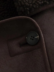 Detail view of a black resin button on dark coffee faux suede shearling winter jacket