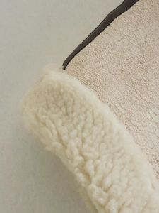 Detail view of winter fleece vest with plush beige texture and brown leather piping edges