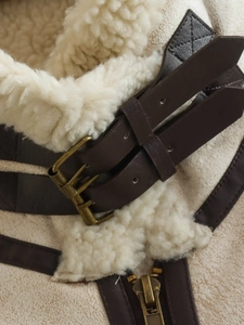 Detail of faux suede vest showing white sherpa lining and brown leather neck straps
