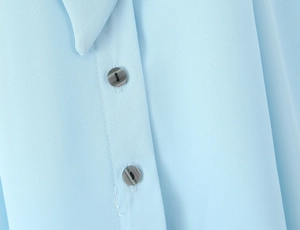 Detail of light blue sleeveless top showing textured fabric and dark grey round buttons