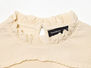 Detail of smocking texture and ruffled neckline on cream slim-fit women shirt