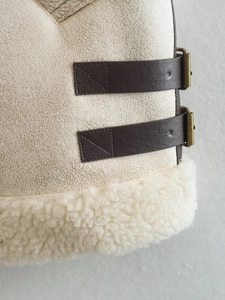 Detailed close-up of sherpa-lined vest featuring brown faux leather straps and vintage buckles