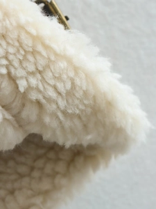 Close-up of thick off-white sherpa fleece texture with vintage gold metal buckle detail