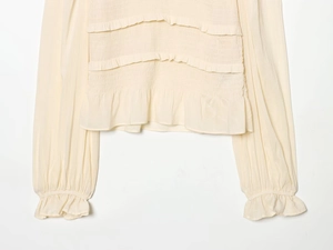 Detailed view of layered ruffles and smocked texture on this cream long sleeve top