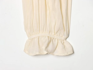 Close-up of ruffled elastic cuffs and pleated fabric texture on off-white slim top