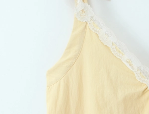 Close-up of delicate white lace trim and stitching on light yellow cotton V-neck dress