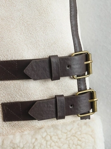Detail of faux shearling vest featuring brown leather straps and bronze metal buckles