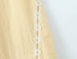 Detail of yellow fabric featuring intricate white floral lace trim and natural texture