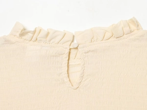 Detailed close-up of smocked beige top neck with ruffle trim and back button closure