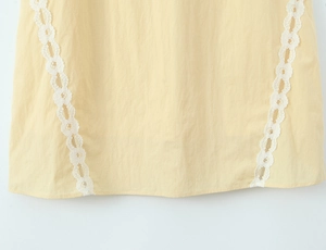Detail of light yellow dress with white floral lace trim on textured cotton fabric