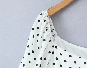 Detail des gerafften Ausschnitts eines weiß-schwarzen Polka-Dot-Kleides am Holzbügel