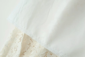 Close-up of white woven fabric with cream lace trim showing intricate overlock stitching