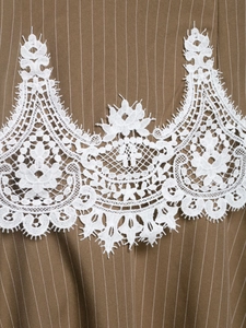 Detailed close-up of white floral lace embroidery on brown pinstripe fabric texture