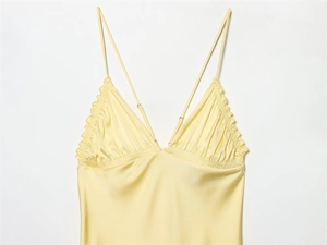 Detail of ruffled V-neckline and dual straps on glossy yellow satin dress for women