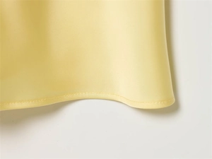 Detailed close-up of smooth satin fabric hem with fine stitching on yellow dress