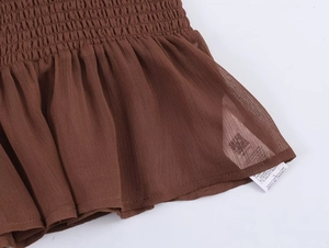 Close-up of smocked brown fabric with ruffled hem and product care label detail
