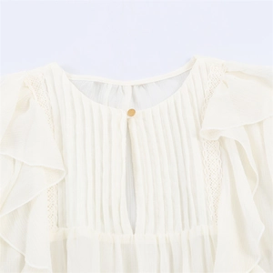 Detail of cream chiffon blouse featuring lace trim, pleated chest, and a single gold button