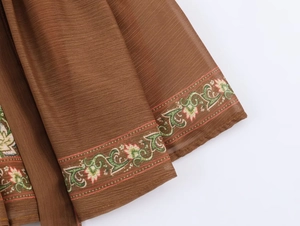 Detailed macro view of brown vintage fabric featuring green vines and pink floral embroidery
