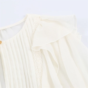 Detail of ruffled shoulder with lace trim and gold button on elegant white chiffon shirt